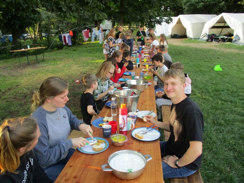 Holztische und -bänke als Ort der Zusammenkunft: Eine Essensgemeinschaft trifft sich zum gemeinsamen Mahl.